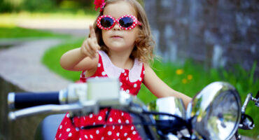Beautiful little girl in a red dress on a motorcycle